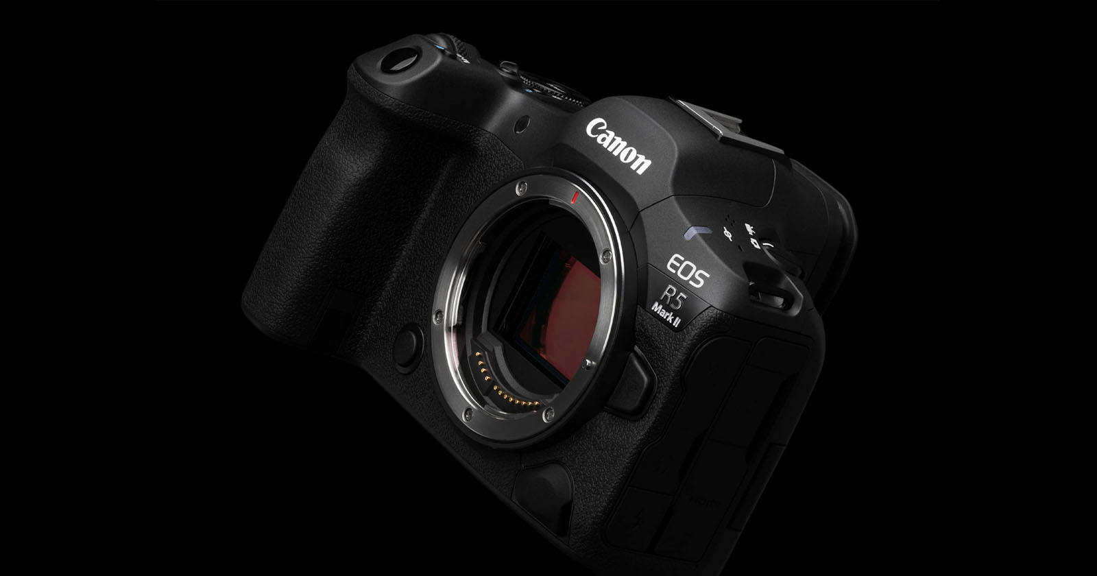 A Canon EOS R5 mirrorless camera is presented against a black background. The camera is angled slightly to the left and forward, displaying the lens mount opening and various control buttons. The Canon logo is clearly visible on the top right.