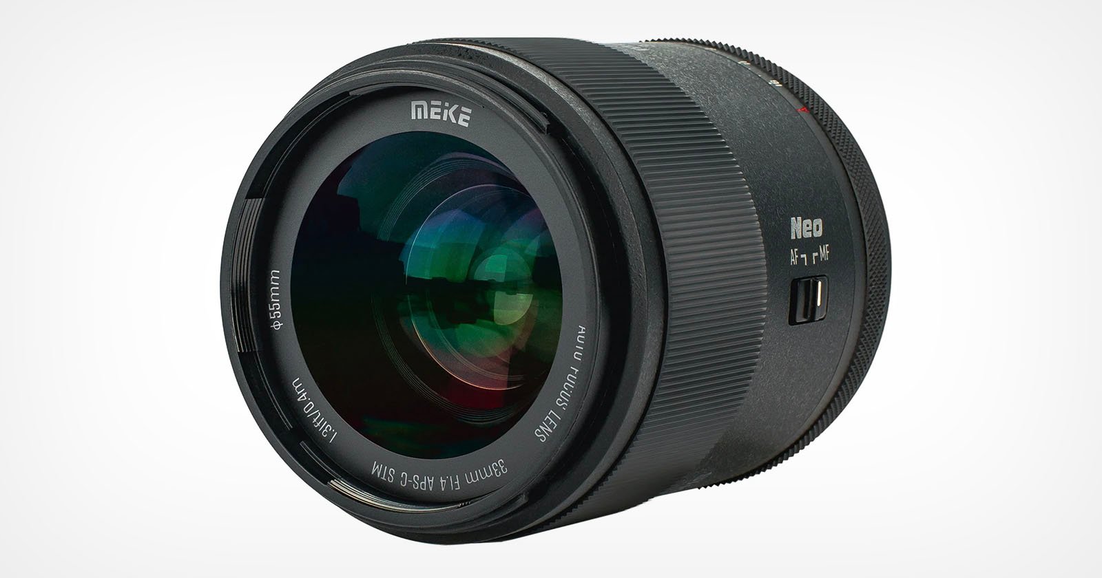 A large camera lens with a sleek black exterior. The lens is labeled MEKE and features various specifications, including 55mm, Auro High Definition, and F1.4. The lens surface reflects light, and there are fine grooves for grip.