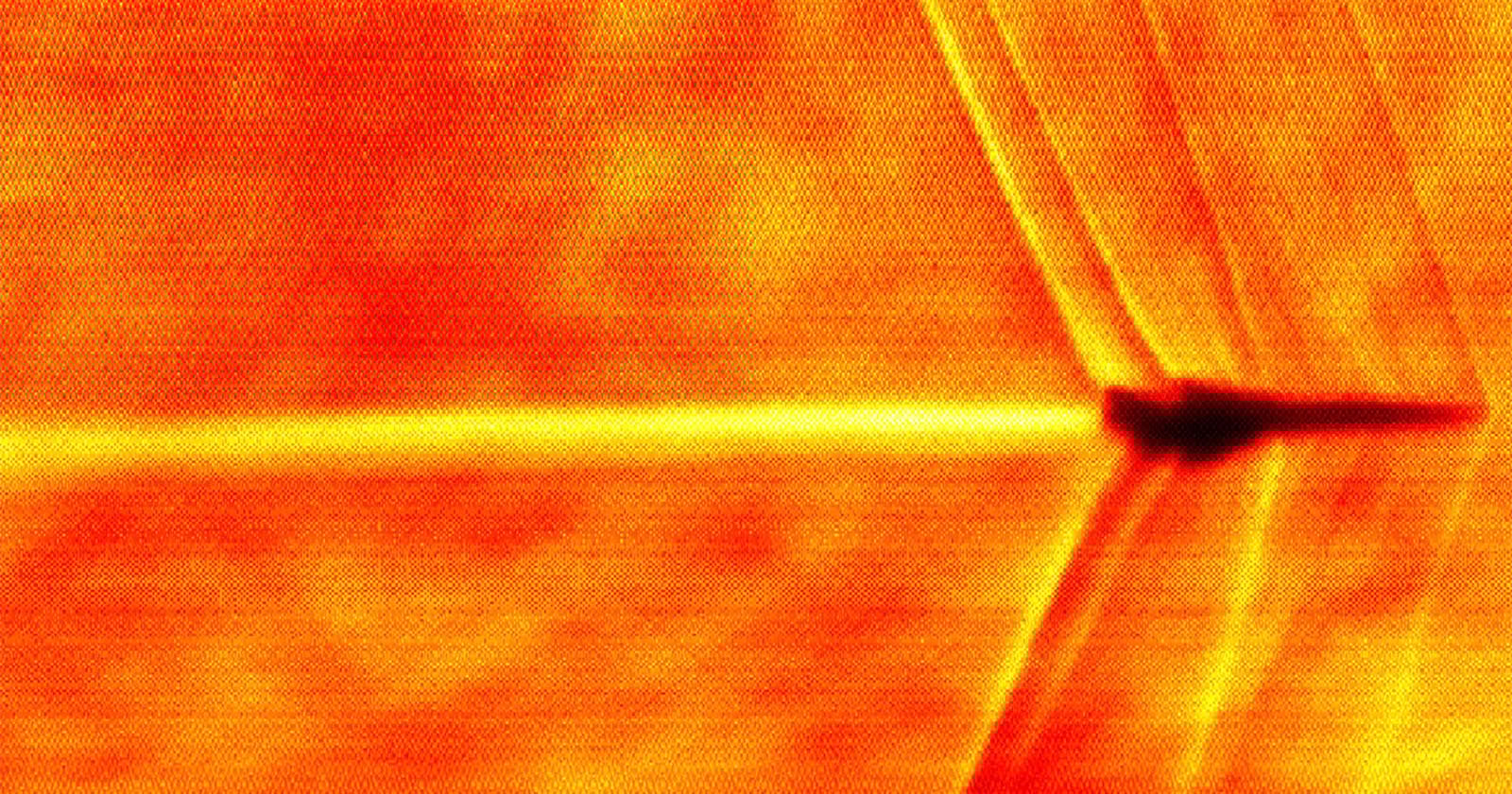 An infrared image of a jet forms a blurry zigzag pattern through the air, with bright orange and red tones indicating heat. The aircraft is in silhouette against the heated background.