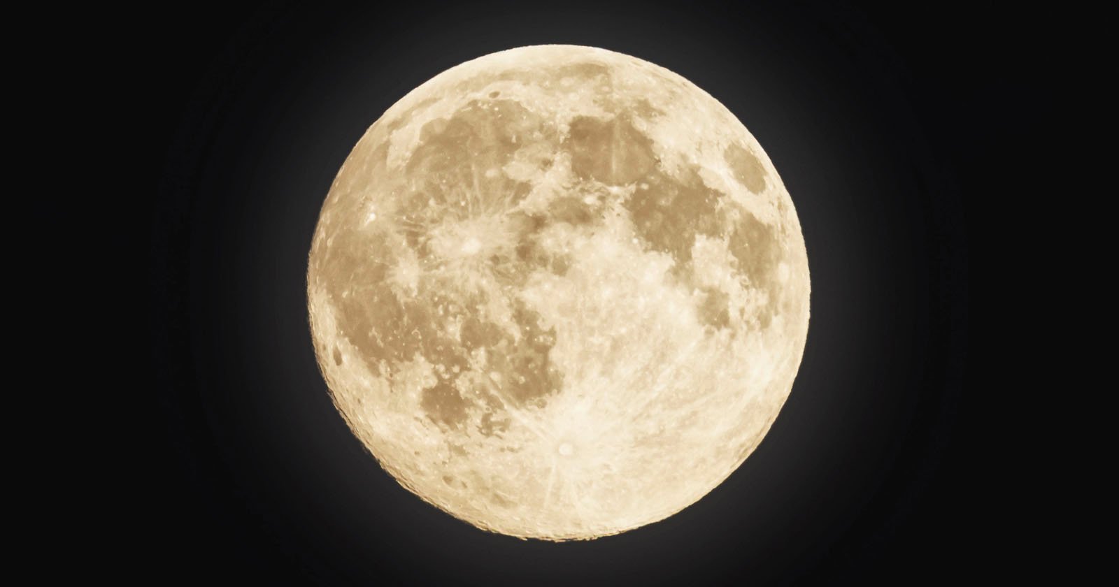 A close-up view of a full moon against a dark night sky, showing detailed craters and surface textures illuminated by bright light.