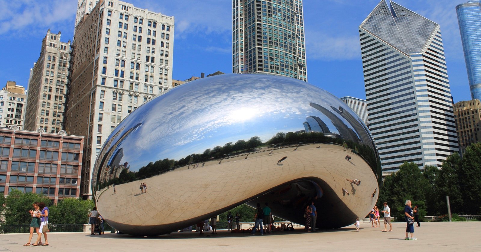 Cloud Gate, also known as The Bean, a large reflective sculpture in Chicago’s Millennium Park, with skyscrapers and blue sky in the background. People are gathered around and beneath the sculpture.
