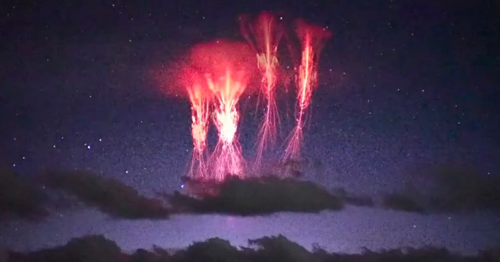 Bright red lightning-like sprites appear above dark clouds in the night sky, with stars faintly visible in the background. The glowing red tendrils stretch vertically, creating an ethereal effect.