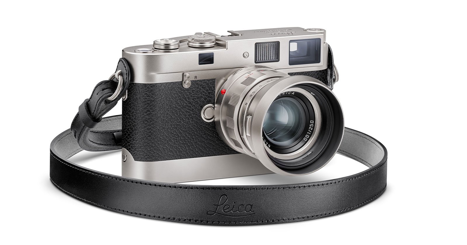 A Leica camera with a silver body and a black textured grip, featuring a large lens and a black leather strap embossed with Leica. The camera is angled to show both the lens and the top dials with a vintage aesthetic.