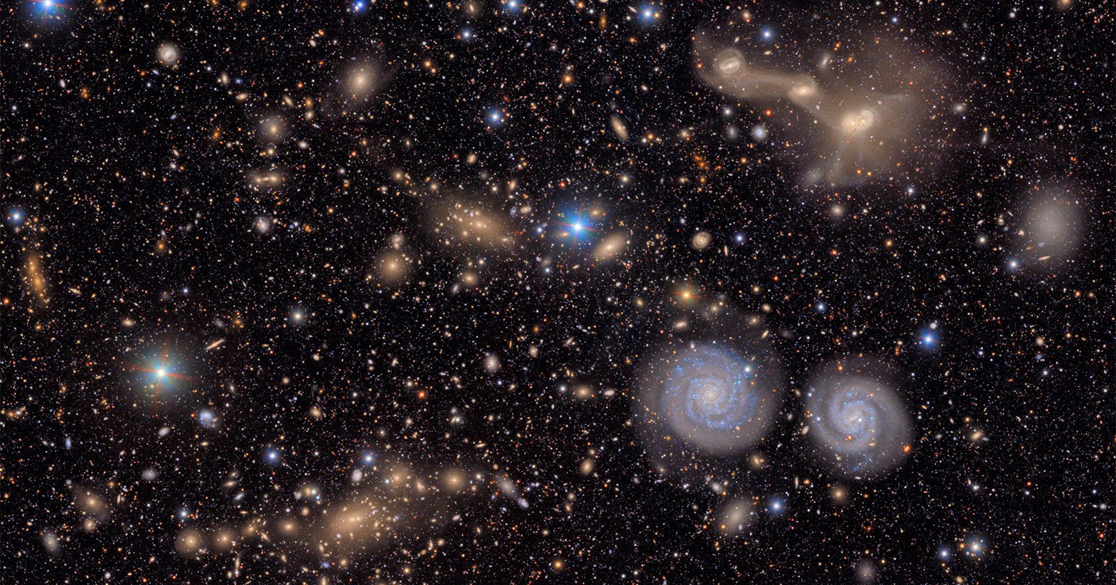 A dense field of stars and galaxies in deep space, featuring two prominent spiral galaxies near the lower right. Various shapes and colors of galaxies are scattered across a dark background.