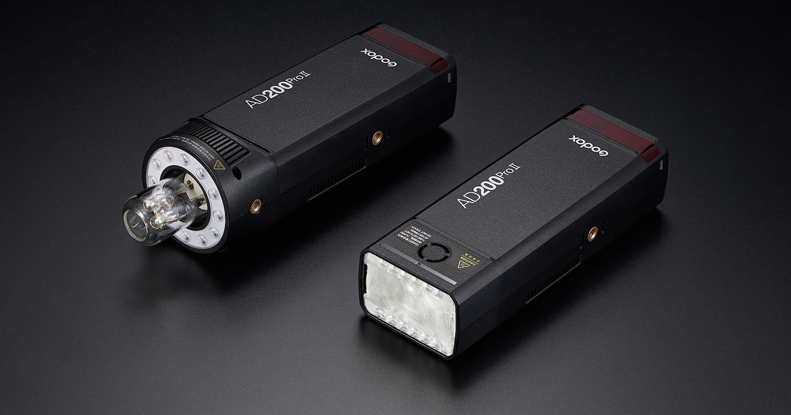 Two Godox AD200Pro portable flash units are displayed on a dark surface. One unit is shown with a bare bulb head, while the other features a rectangular LED head. Both flashes are prominent and accompanied by AD200Pro and Godox branding on their bodies.