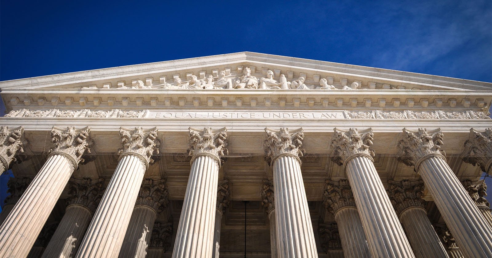 The image shows the facade of the U.S. Supreme Court building, featuring six large Corinthian columns supporting a triangular pediment. Engraved above the columns is the phrase EQUAL JUSTICE UNDER LAW. Figures are sculpted in the pediment, set against a clear blue sky.