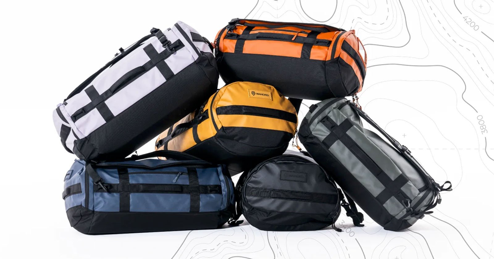 A stack of six durable duffel bags in various colors, including white, orange, yellow, black, blue, and green, are arranged on a white background with a faint topographic map design. The bags feature black straps and zippers.
