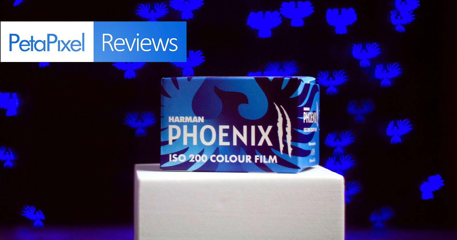 A box of Harman Phoenix ISO 200 Colour Film sits on a white platform against a dark background with blue abstract shapes, with a PetaPixel Reviews banner in the top left corner.