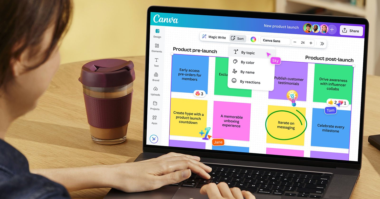 A person uses a laptop displaying a colorful project management board on Canva. The board includes sections for pre-launch and post-launch tasks, with sticky notes, tasks, and names like June and Tom. A reusable coffee cup is beside the laptop.