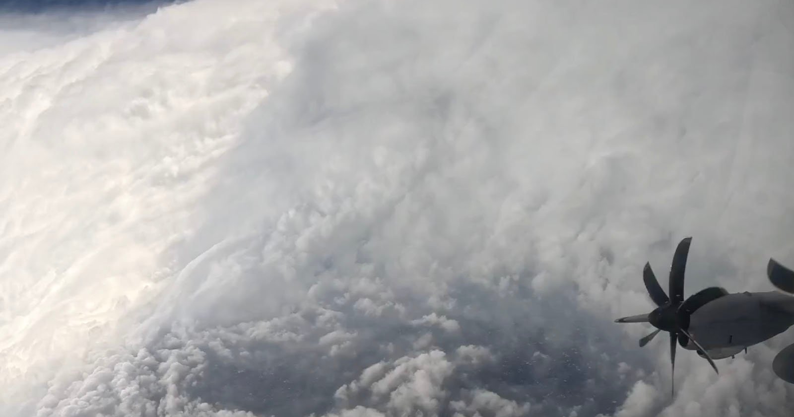 Aerial view from an aircraft flying near the edge of a dense, swirling hurricane, with the aircraft’s propeller visible on the right side and thick clouds dominating the scene. Aerial view from an aircraft flying near the edge of a dense, swirling hurricane, with the aircraft’s propeller visible on the right side and thick clouds dominating the scene.