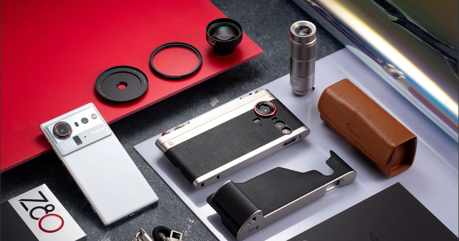 A flat lay photo of a stylish camera with accessories, including lenses, filters, a grip, a leather case, a strap, a metallic tube, and a box labeled “Z80,” all arranged on a surface with red and white paper.