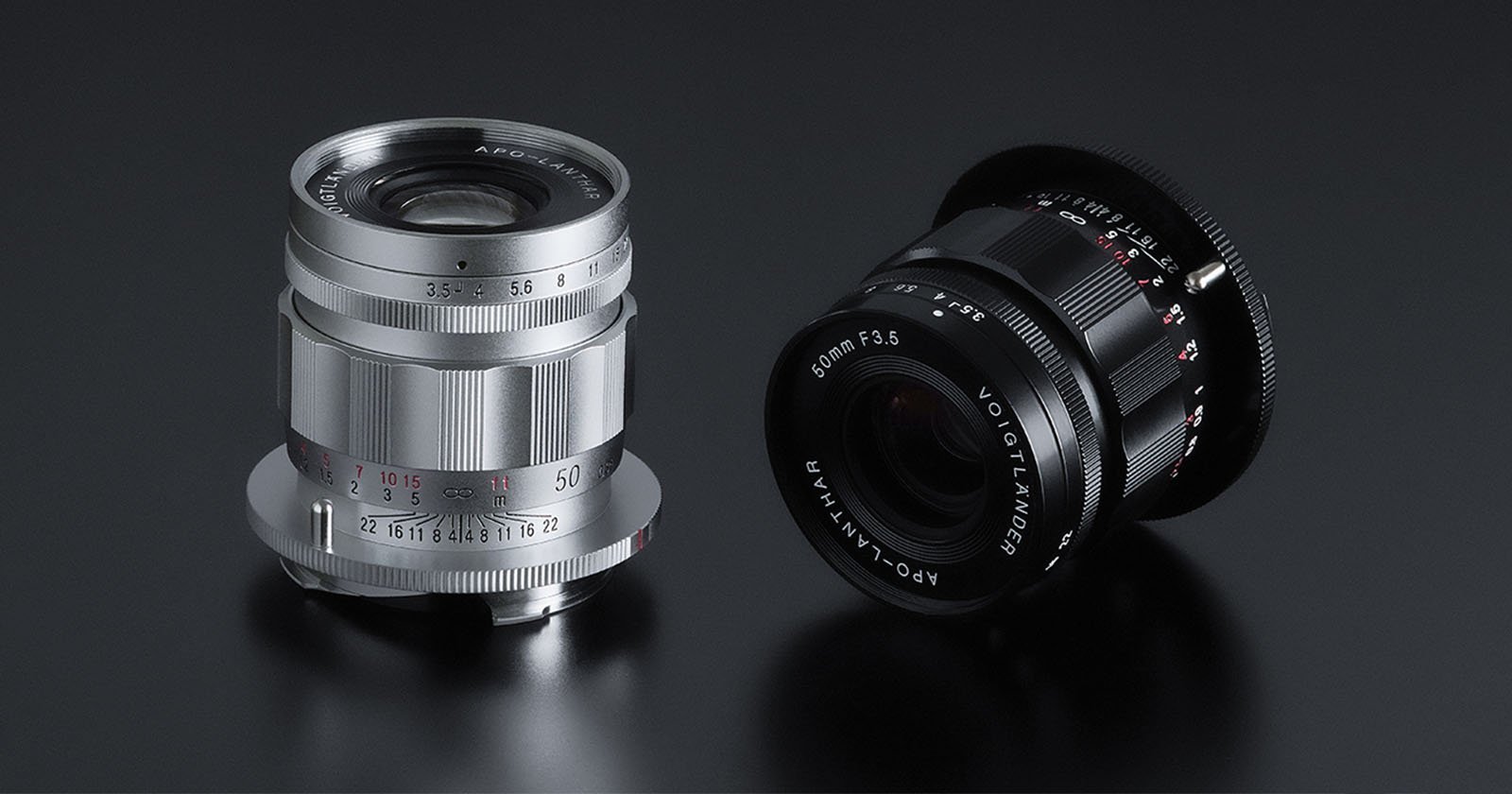 An image showing two camera lenses on a dark, reflective surface. The lens on the left is silver with white and red markings, while the lens on the right is black with white markings. Both lenses have Voigtländer branding visible on them.