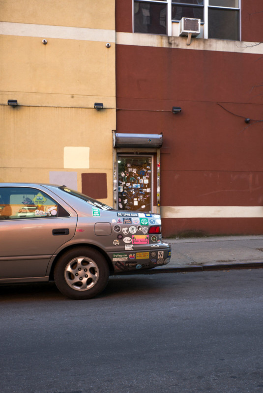 A car with stickers parked in front of a building with stickers
