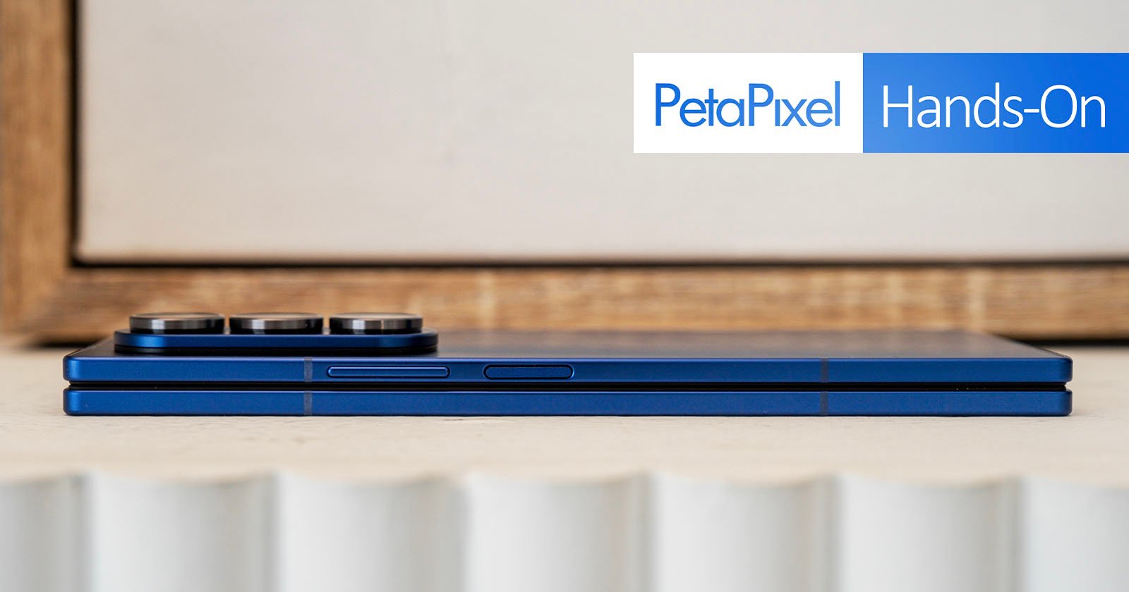 A blue foldable smartphone shown closed and viewed from the side, with camera lenses visible. The image features PetaPixel Hands-On text in the upper right corner.
