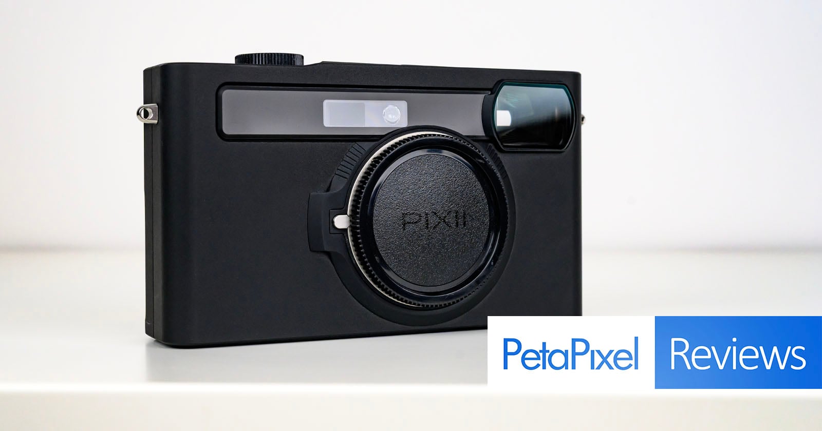 A black PIXII camera sits on a white surface, with the PetaPixel Reviews logo displayed in the bottom right corner of the image.