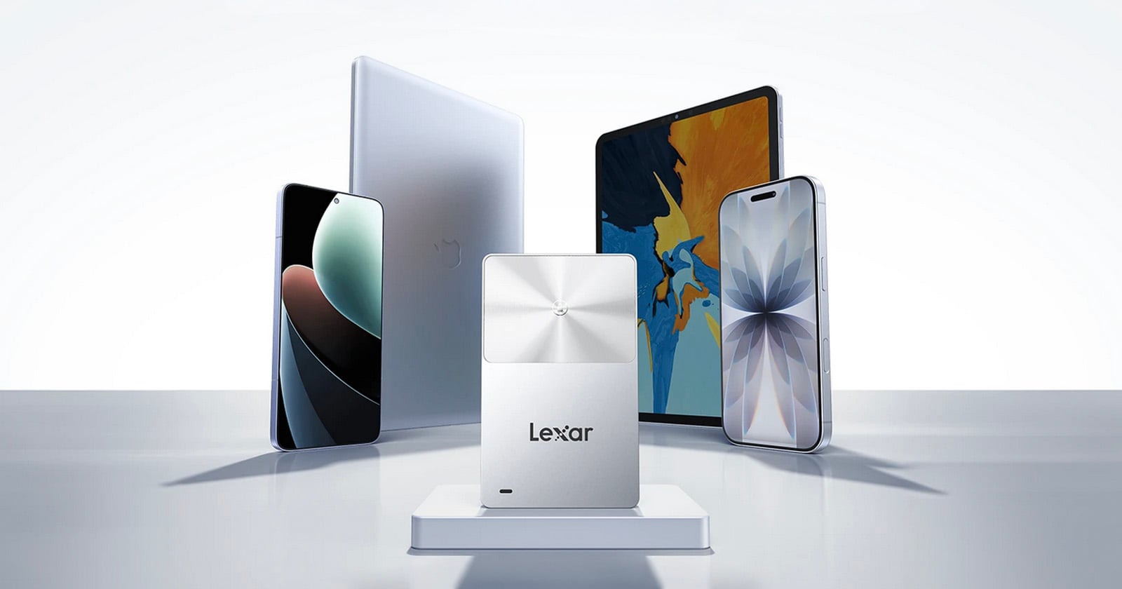 A silver Lexar external solid-state drive is displayed in front of a smartphone, a tablet, and a laptop, all positioned on a white surface with a minimalist background.