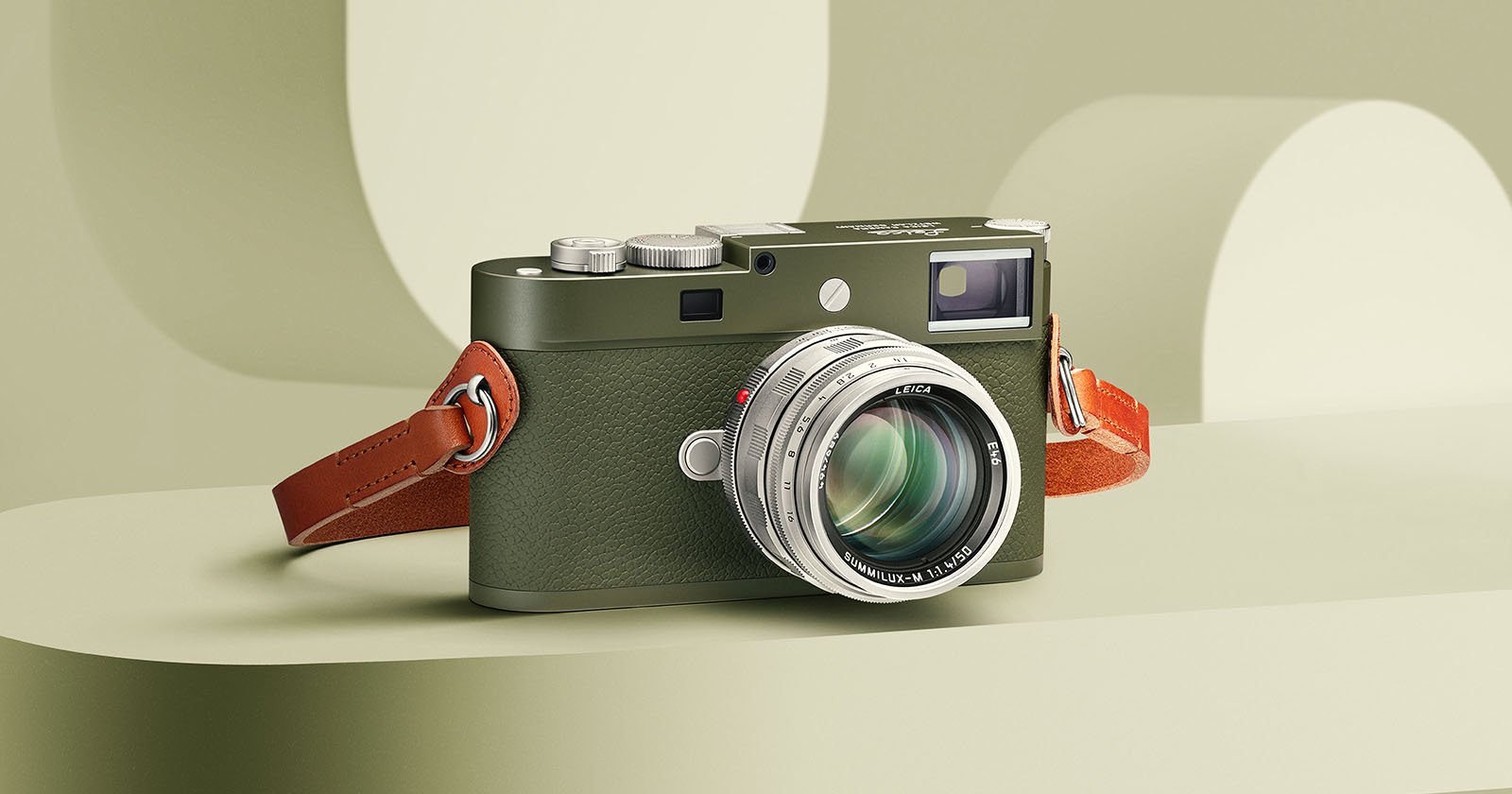 A green and silver digital camera with a brown leather strap is displayed on a pale green surface, with a soft-focus geometric background in similar tones.