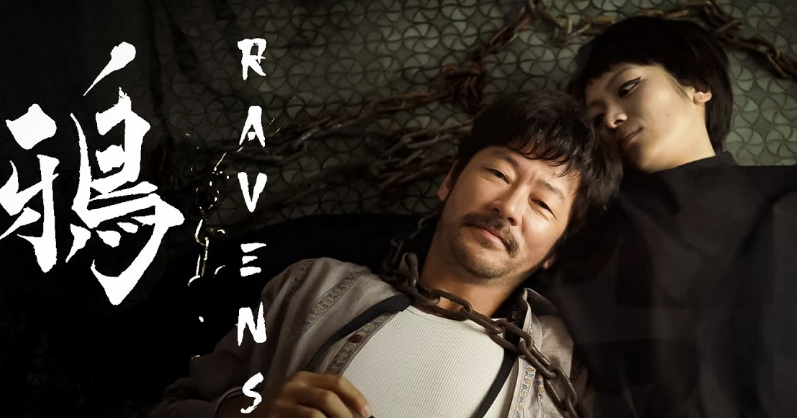A man and a woman lie on the ground, with the man's head resting on the woman's shoulder. Chains are visible around the man's neck. The word Ravens and stylized characters are displayed on the left.