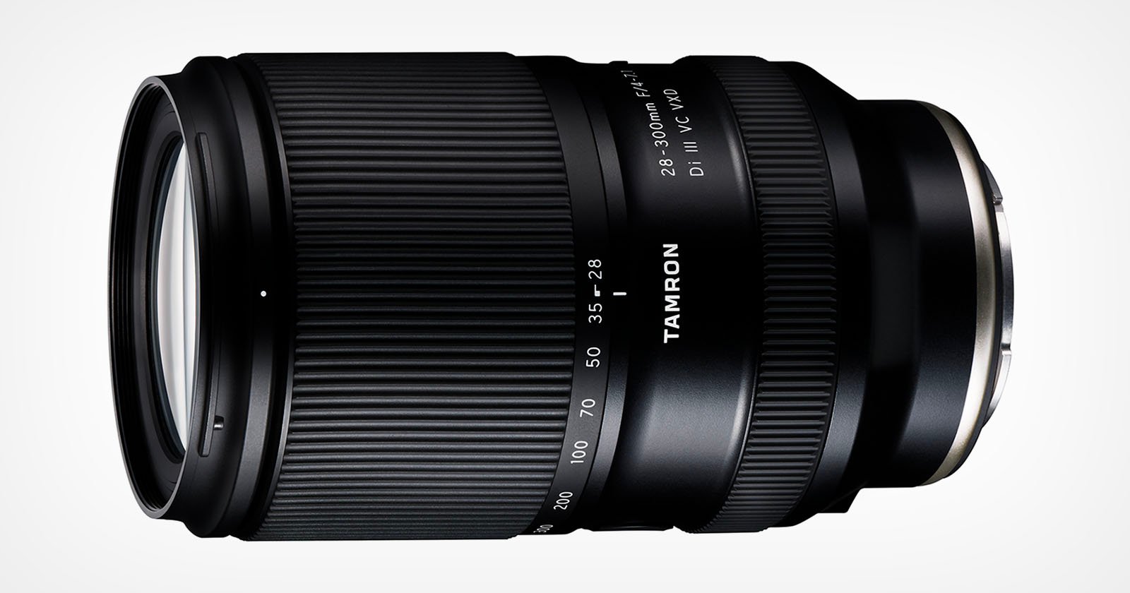 A black, cylindrical camera lens with various zoom settings marked on its body. The brand Tamron is visible on the side, and the lens details 28-300mm F/3.5-6.3 Di II VC PZD are also displayed. The lens has a ridged, textured grip for manual adjustments.