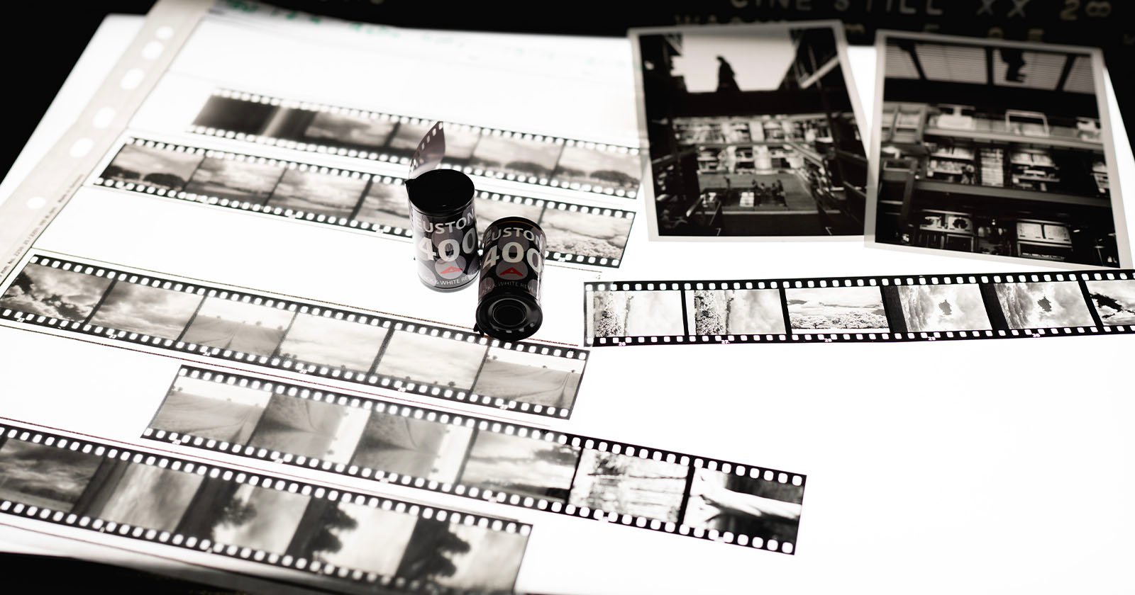 Black and white photo negatives, film canisters, and two printed photographs are displayed on a lightbox, showcasing various urban and landscape scenes.