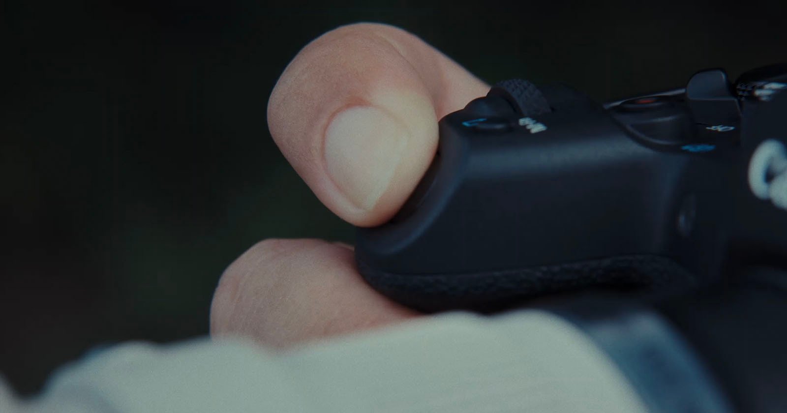 A close-up of a person's hand holding a black game controller, with their thumb resting on one of the buttons.