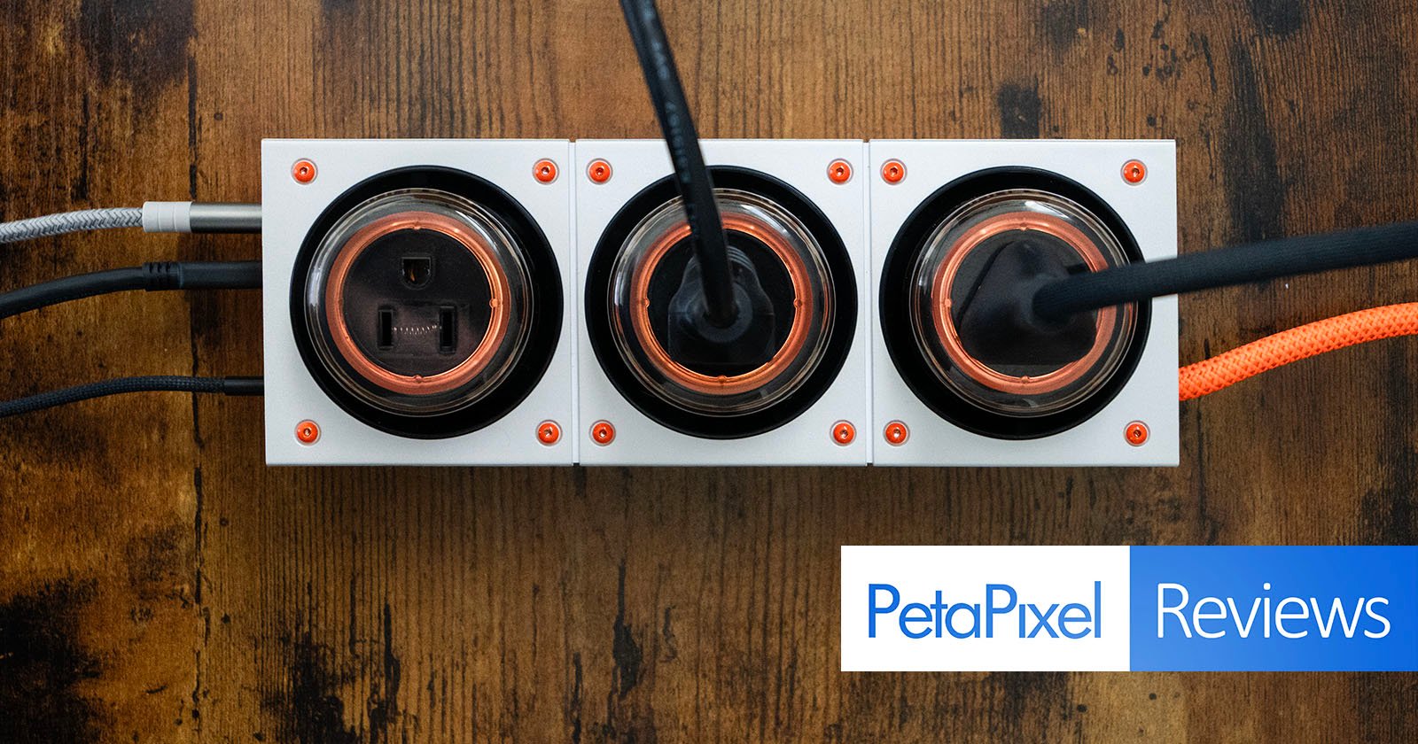 A top-down view of three modern electrical outlets with cords plugged in, mounted on a wooden surface. The Petapixel Reviews logo appears in the bottom right corner.