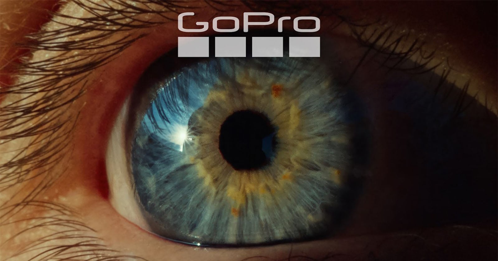 A close-up of a blue and amber human eye with a reflection visible in the pupil. The GoPro logo and four squares are positioned above the eye.