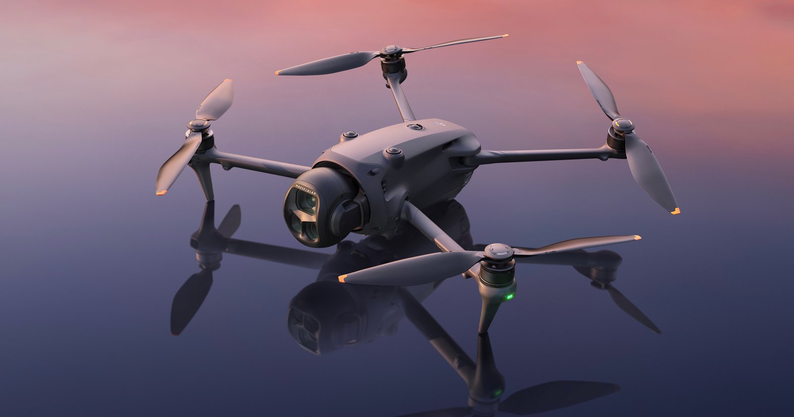 A close-up of a sleek, modern quadcopter drone with four propellers, resting on a smooth reflective surface under a soft pink and purple sky.