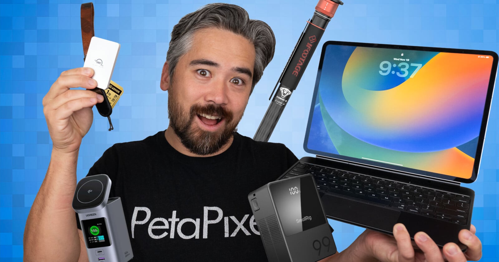 A smiling man in a PetaPixel shirt holds various tech gadgets, including an external drive, a camera, a battery, a tripod, and an Apple iPad with a keyboard, against a blue geometric background.