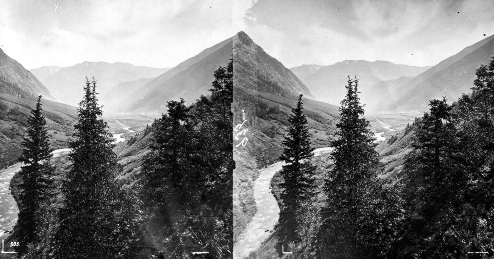 Stereoscopic view of a lush mountain valley with a river running through it and coniferous trees in the foreground; rugged mountain peaks rise in the background.