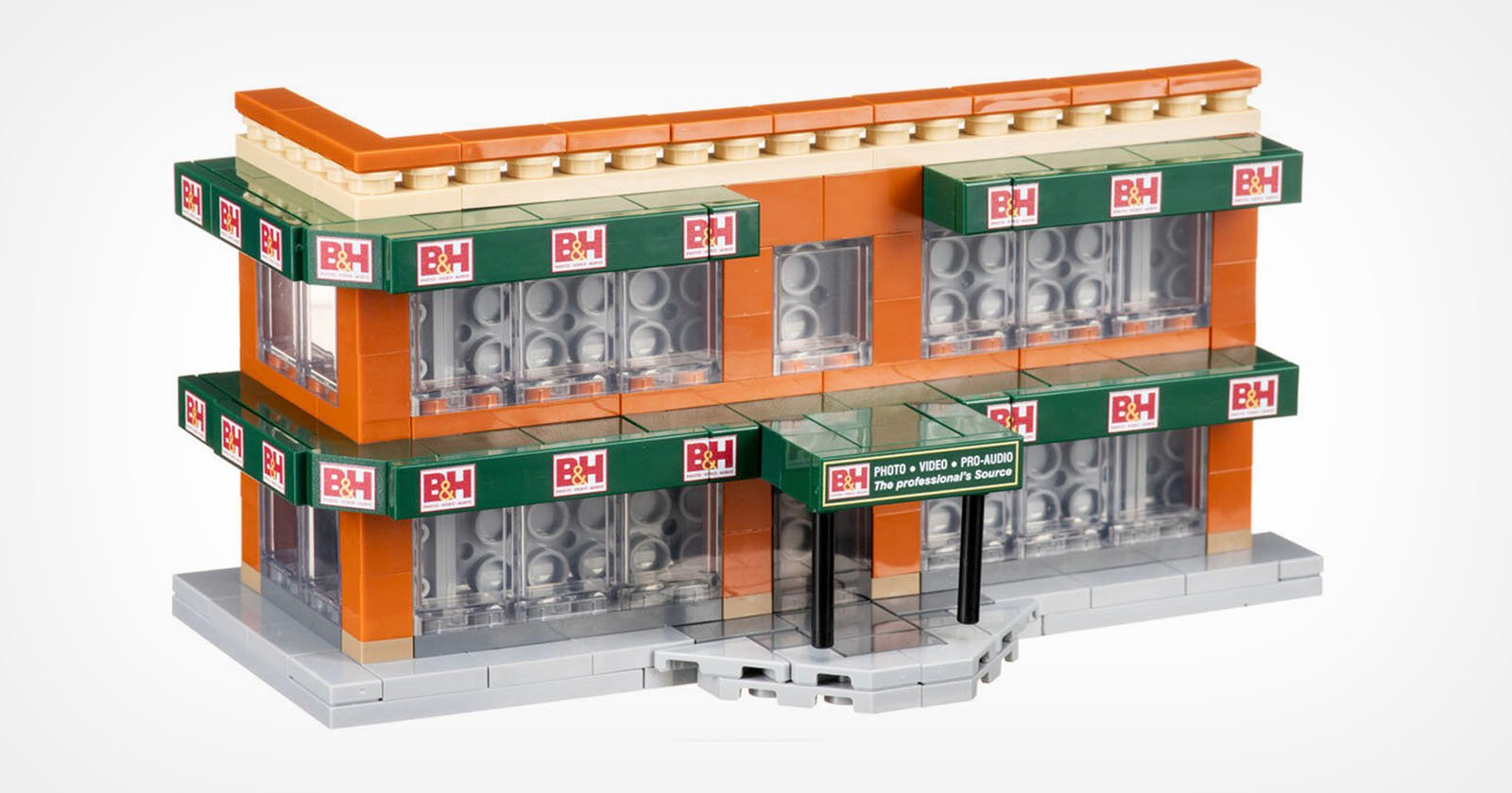 A Lego model of a two-story building with green B&H signage on multiple sides. The building features orange walls, large windows, and a small overhang above the entrance. The base is gray, mimicking a sidewalk.