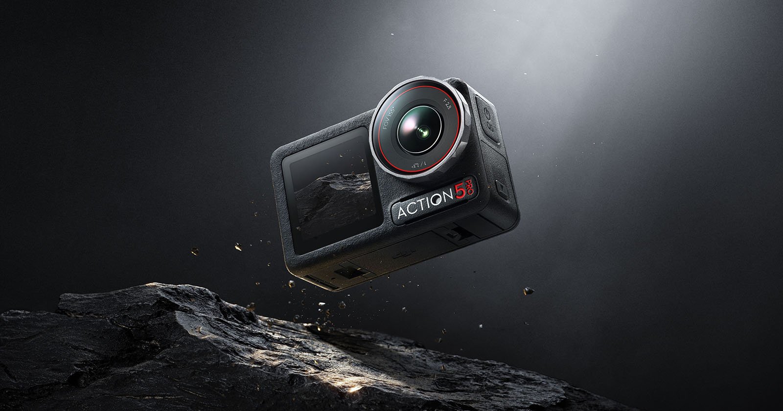 A rugged black action camera labeled ACTION with a lens and display is suspended mid-air above a rocky surface, illuminated by a directed light from above. Dust particles float around it, highlighting its robust and adventure-ready design.