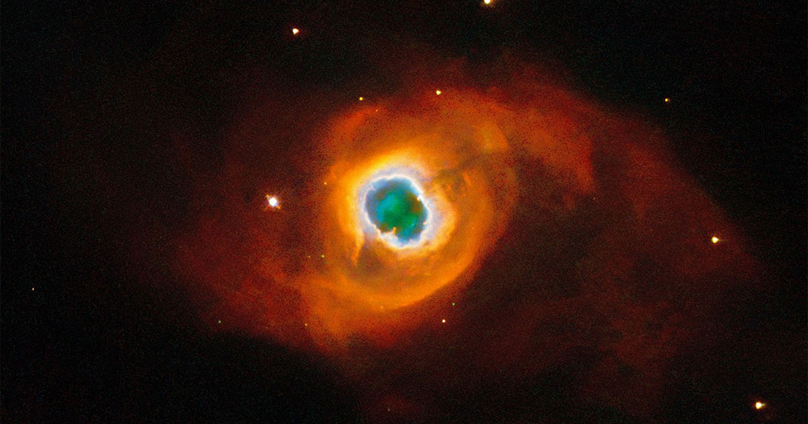 Bright nebula in space, showing vivid orange and red clouds surrounding a luminous blue and white center. Small distant stars are scattered across the dark background.