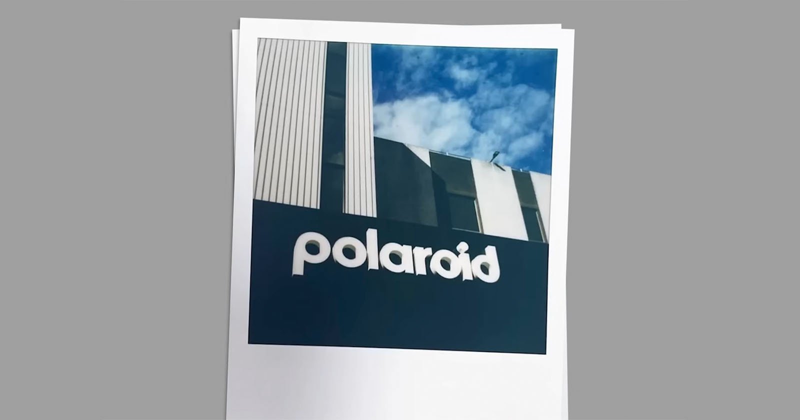 A Polaroid photo of a building with the word polaroid on it. The building features a modern design with vertical lines and a mix of white and dark colors. The sky is partly cloudy in the background.