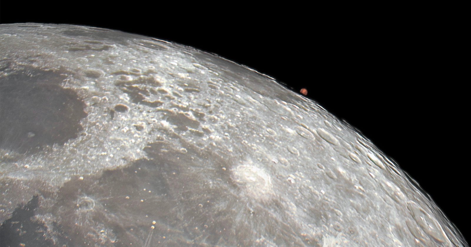 Close-up of the moon's surface showing detailed craters and textures. In the background, a small reddish celestial object, likely a planet or a star, appears on the horizon against a black sky.