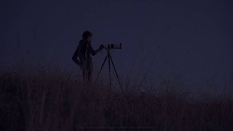A man standing with a camera on a tripod at night