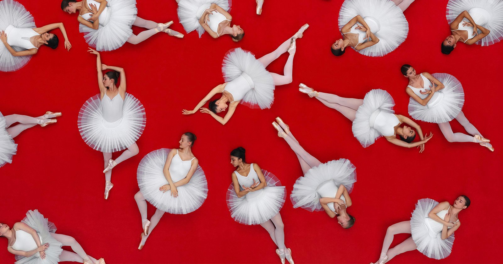 Ballet dancers in white tutus and pointe shoes pose gracefully on a vibrant red background, arranged in various elegant positions viewed from above.