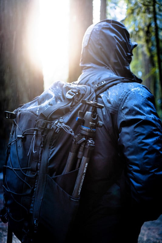 A photographer wearing a backpack with a tripod strapped to it