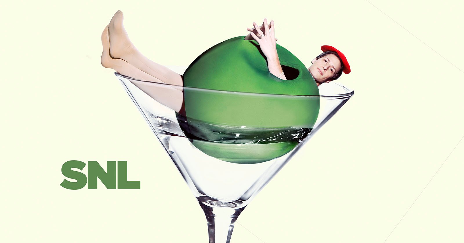 A person wearing a red beret playfully emerges from a large green olive in a martini glass. The background is light, and the SNL logo is at the bottom left.