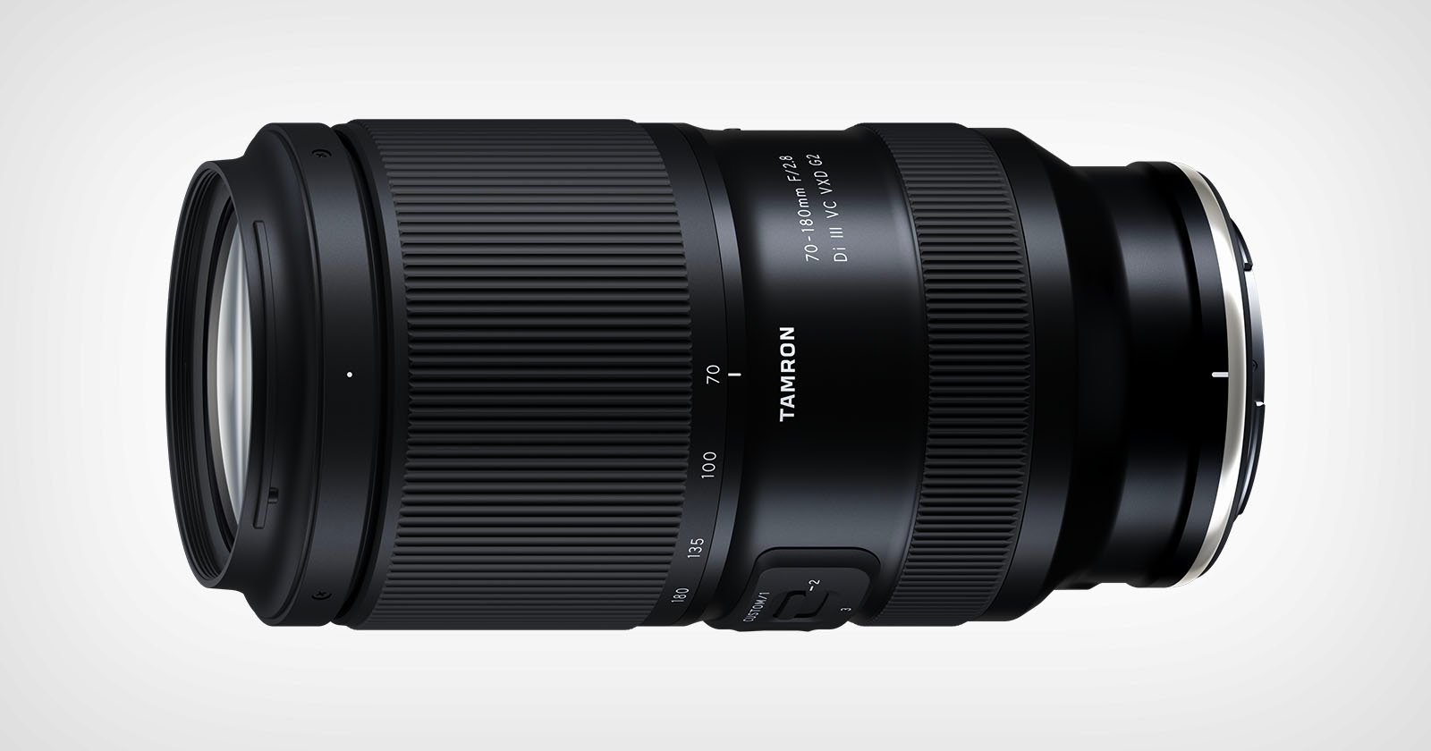 A black Tamron camera lens with zoom and focus rings, labeled 70-180mm F/2.8 Di III VXD, lying horizontally on a light background.