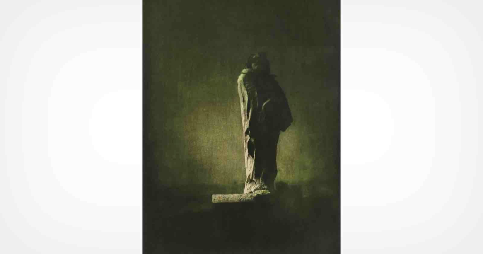 A dark, moody image of a stone statue standing on a pedestal, shrouded in shadow and mist, with a somber and mysterious atmosphere.