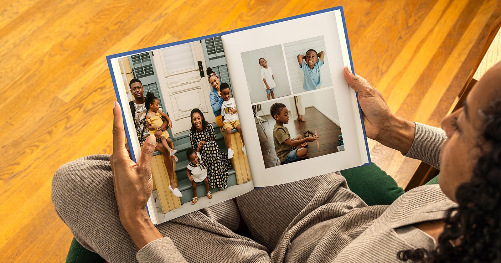 A person holds an open photo book featuring family photos. The left page shows a family sitting together, while the right page displays individual pictures of children in various poses, set against a wooden floor background.