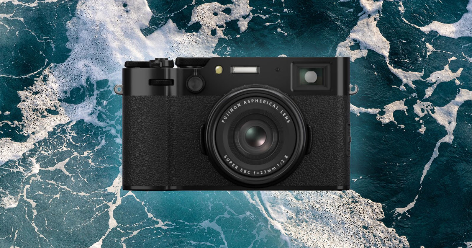 A black digital camera with a textured grip is centered over a background of ocean waves with white foam.