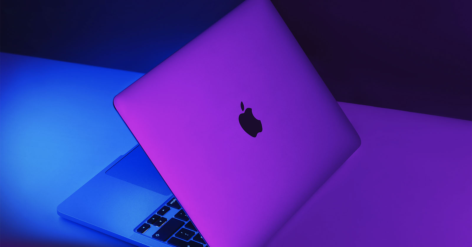 A photo shows a MacBook illuminated by purple lighting.