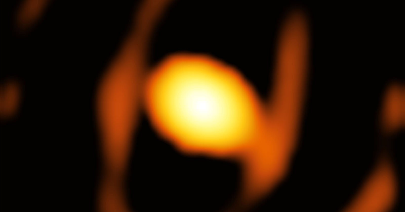 A blurred, glowing orange orb is surrounded by darker, abstract shapes on a black background, resembling a celestial object or distant light source.
