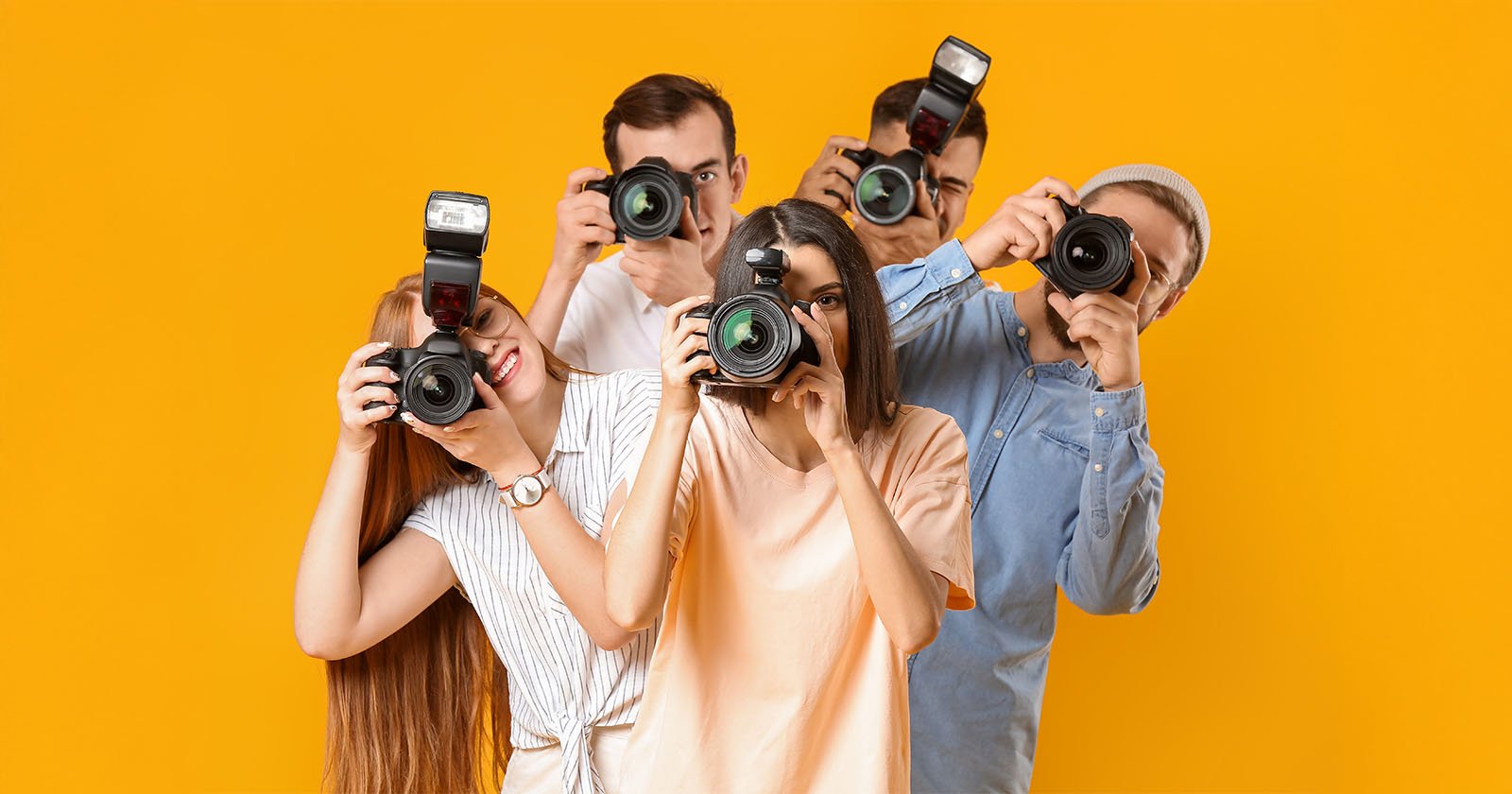 Five young adults stand close together against a bright yellow background, each holding a camera up to their face as if taking a photo. They appear cheerful and engaged in photography.