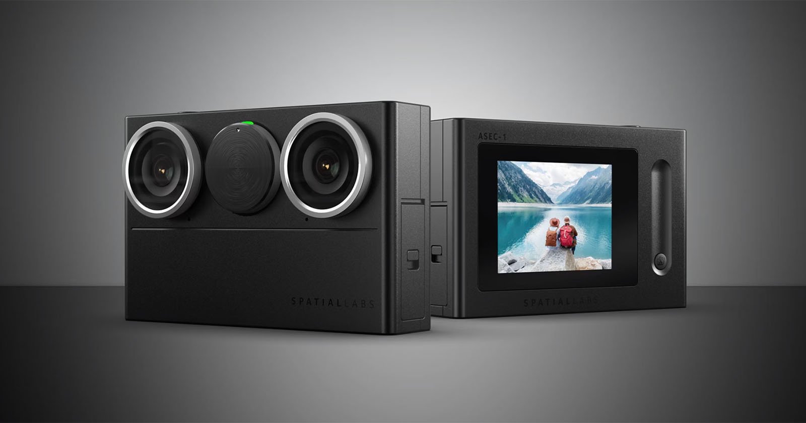 A dual-lens camera sits on a gray surface. The device has two circular lenses on the front and a viewfinder screen on the back displaying a picture of a person and a dog near a lake with mountains in the background. The brand name SPATIAL LABS is visible.