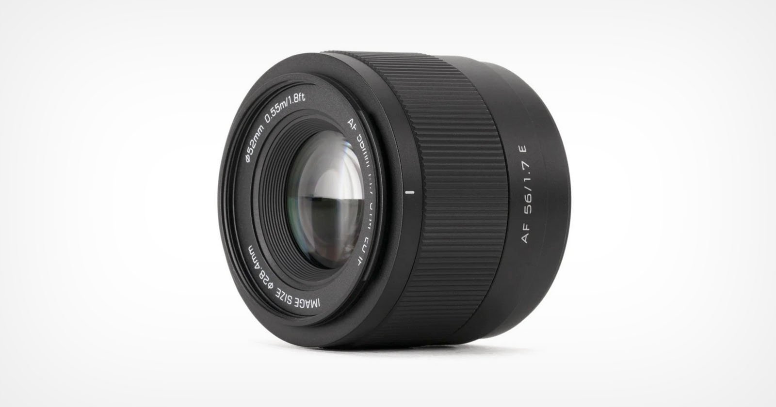 A black camera lens with markings indicating it is an AF 56mm f/1.7 E model. The lens has a textured focus ring and a glass element at the center. The background is white, highlighting the lens's details.