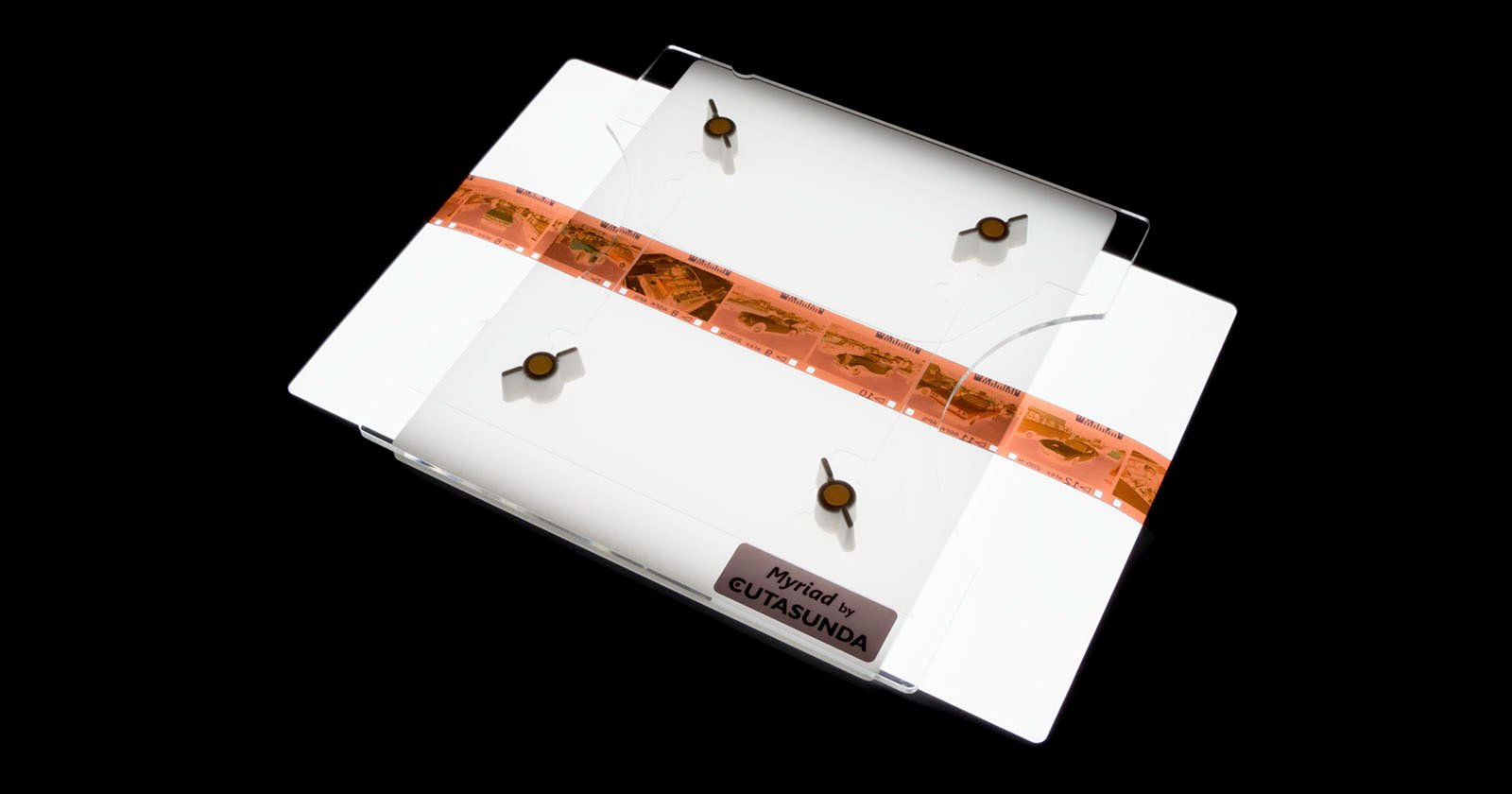 A transparent, rectangular object with a brown band across the middle, bearing small text and symbols. Four suction cup-like attachments are on the corners, and the bottom is labeled EUTASUNDA. Set against a black background.