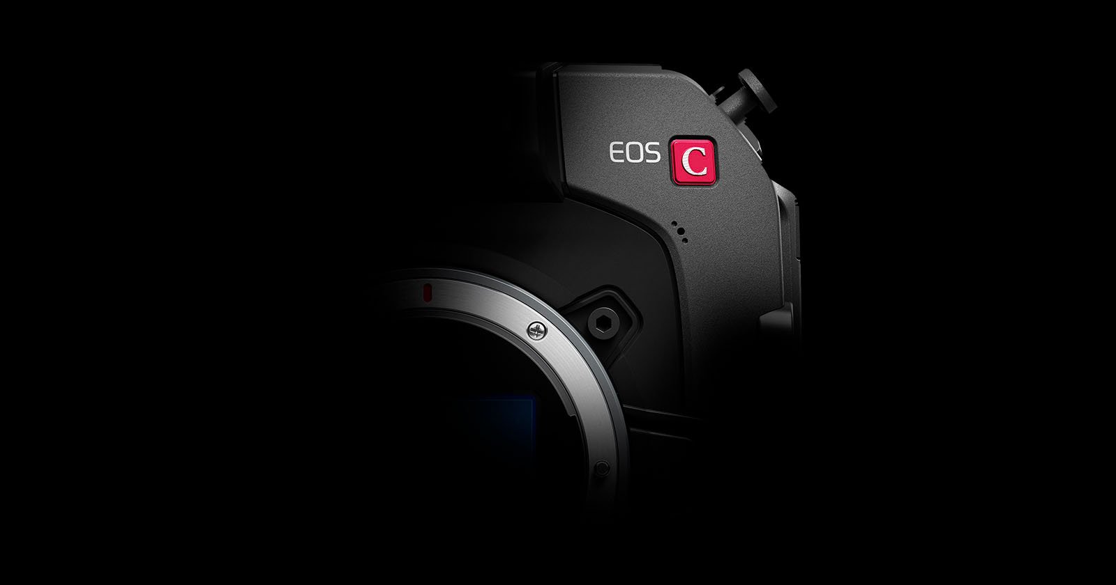 A partially lit camera against a black background, showing the EOS C label and part of the lens mount area. The rest of the camera body fades into the darkness.